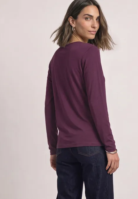 T-shirt basique uni à manches longues berry maroon Frau in lila langärmligem Shirt und Jeans blickt über die Schulter.