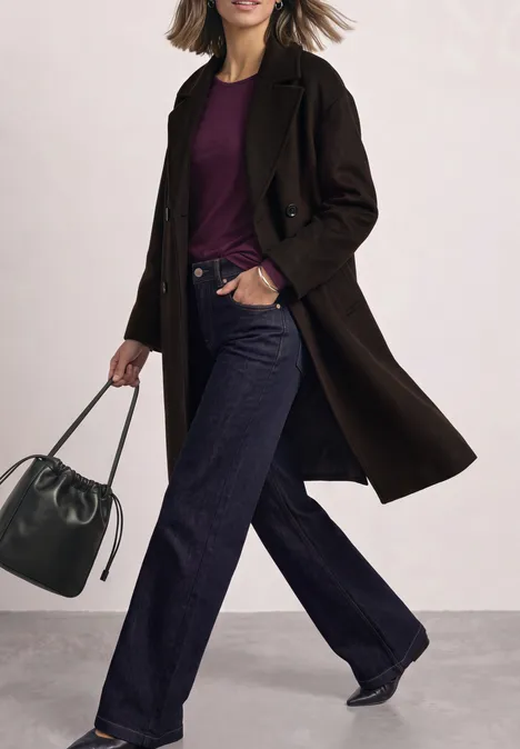 T-shirt basique uni à manches longues berry maroon Frau in dunklem Mantel, lila Shirt, weiten Jeans und Tasche.