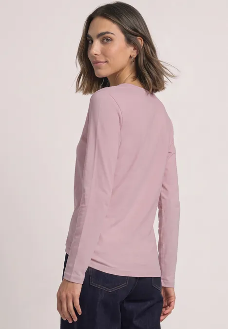 T-shirt basique uni à manches longues quiet rose Eine Frau in rosa Langarmshirt und dunkler Hose steht seitlich und schaut über die Schulter.