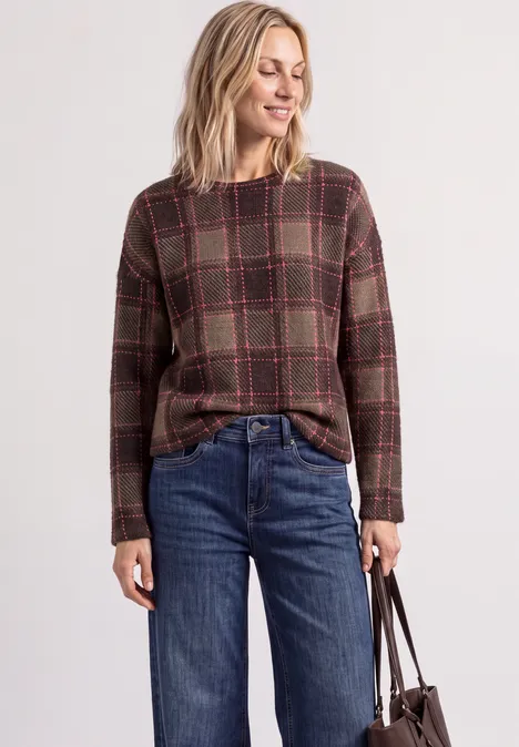 Frau trägt kariertes Langarm-Oberteil, blaue Jeans und hält eine Handtasche.