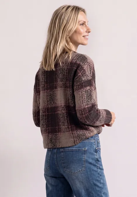 Eine blonde Frau in kariertem Cardigan und Jeans schaut lächelnd seitlich weg.