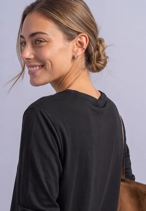 Une femme aux cheveux attachés, vêtue de noir, sourit de côté à l’appareil.