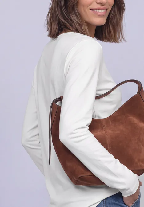 Femme en haut blanc souriante portant un sac en daim marron sur l’épaule.