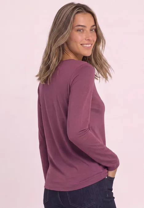 Une femme souriante en tee-shirt manches longues violet regarde par-dessus son épaule.