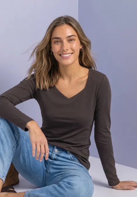 Femme souriante en tenue décontractée assise au sol devant un fond uni.