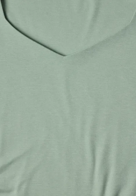 Gros plan sur un tissu vert clair à col en V, texture fine et uniforme.