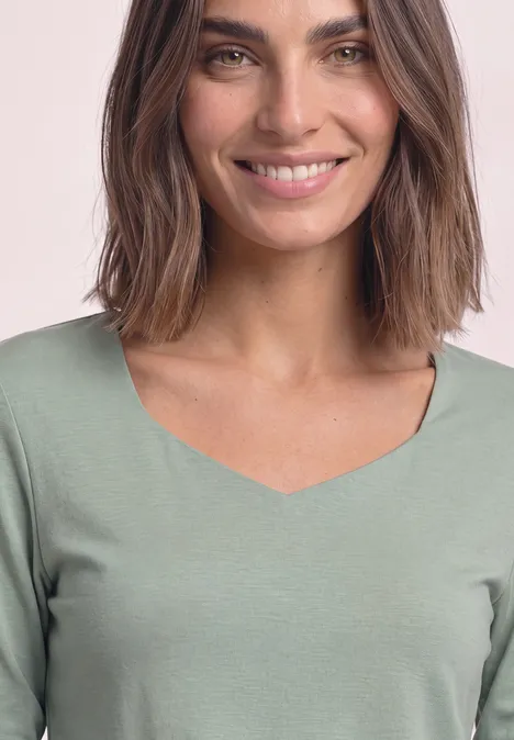 Une femme souriante aux cheveux bruns portant un haut vert à encolure en V.