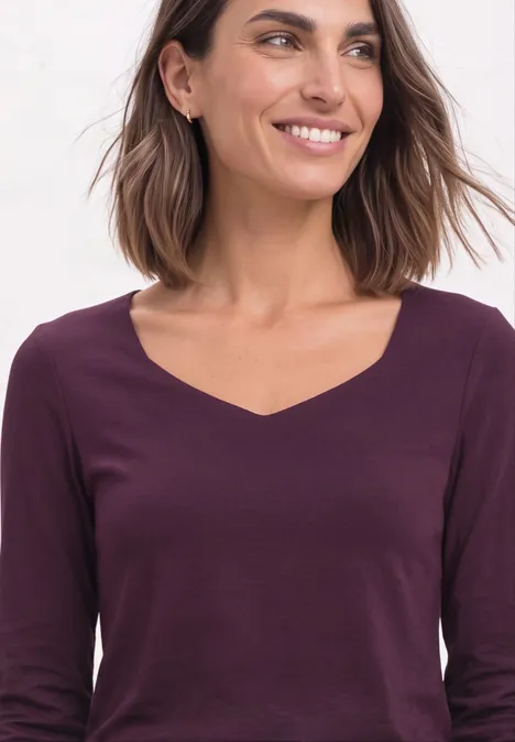 Glimlachende vrouw met bruin haar in bordeauxrode V-hals top.