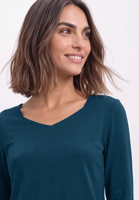 Vrouw met halflang bruin haar glimlacht en draagt een donkergroen V-hals T-shirt.