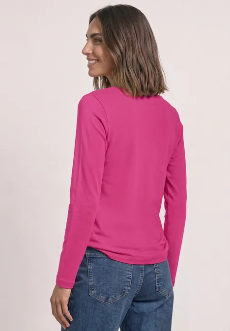 Langarm Shirt mit U-Boot-Ausschnitt magenta dream Eine Frau mit schulterlangem braunen Haar trägt ein pinkes Langarmshirt und blaue Jeans und lächelt seitlich.