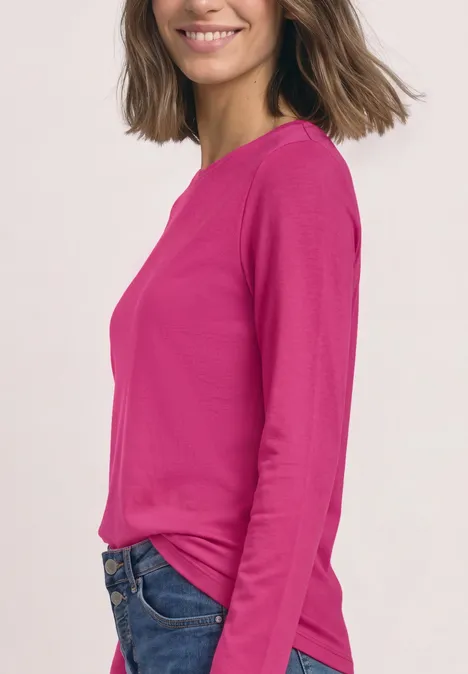 Langarm Shirt mit U-Boot-Ausschnitt magenta dream Frau im pinken Langarmshirt und Jeans, seitlich stehend, lächelnd vor hellem Hintergrund.