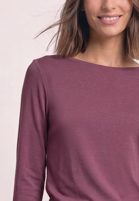 Frau trägt ein langärmeliges, pflaumenfarbenes Shirt mit Boot-Ausschnitt.