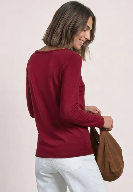 Frau im roten Pullover und weißen Hosen von hinten mit brauner Tasche