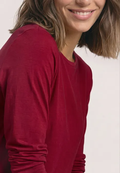Eine Frau mit braunen Haaren in einem roten Langarmshirt lächelt freundlich.