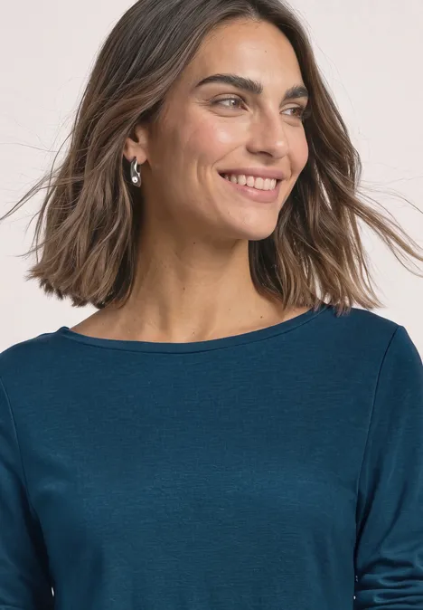 Een glimlachende vrouw met halflang bruin haar en blauw shirt, kijkend opzij.