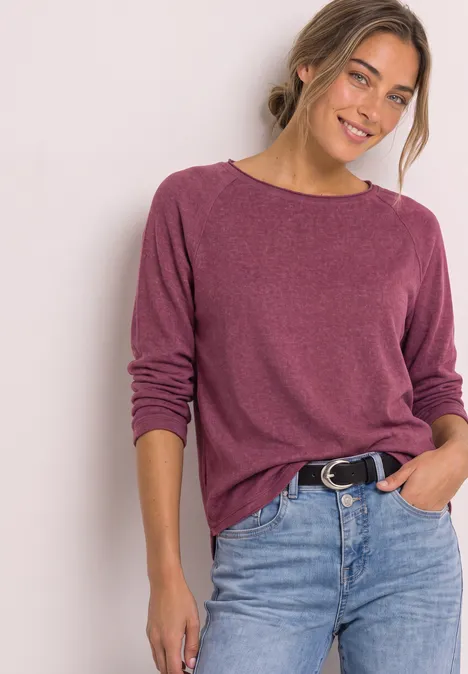 Langarm Shirt mit Rundhals und Rollkante dark clouded blush Junge Frau in violettem Pullover und Jeans, lächelt entspannt, eine Hand in der Hosentasche.