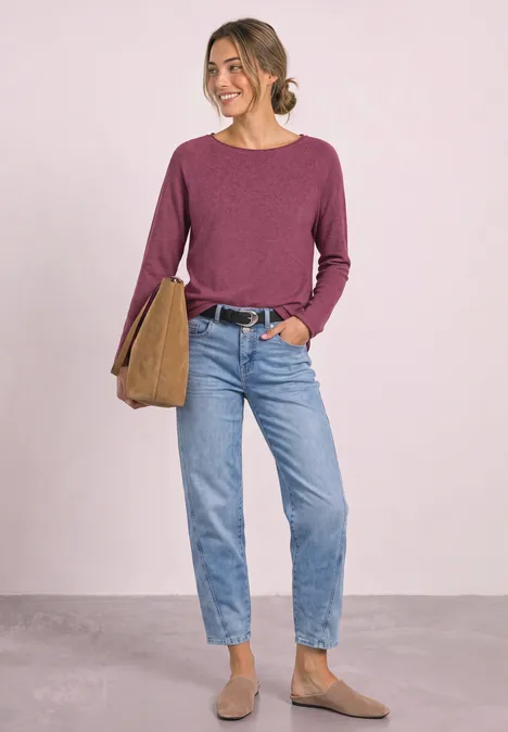 Langarm Shirt mit Rundhals und Rollkante dark clouded blush Frau in lila Pullover, Jeans und braunen Stiefeletten trägt Tasche und lächelt.