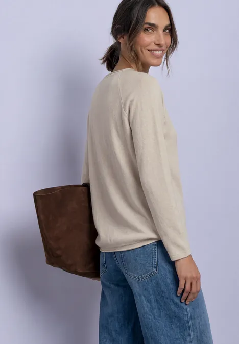 Langarm Shirt mit Rundhals und Rollkante clay sand mel. Eine Frau mit beigem Pullover, Jeans und brauner Tasche blickt lächelnd über die Schulter.