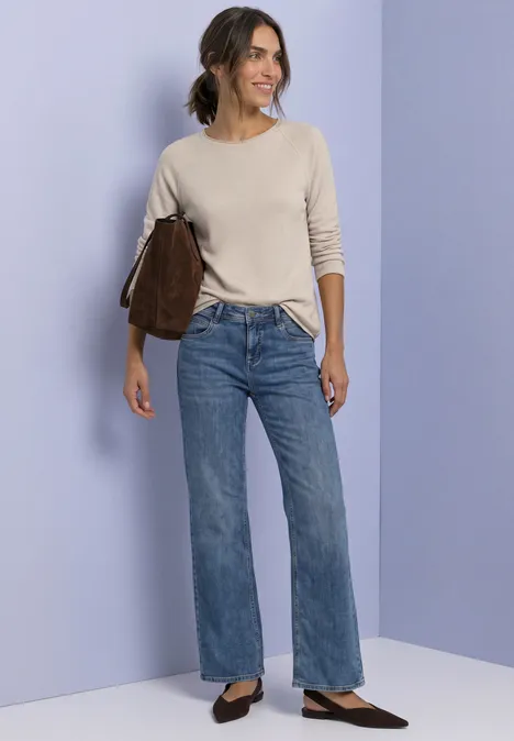 Langarm Shirt mit Rundhals und Rollkante clay sand mel. Eine Frau in beigem Pullover und weiten Jeans mit brauner Tasche vor pastellfarbenem Hintergrund.