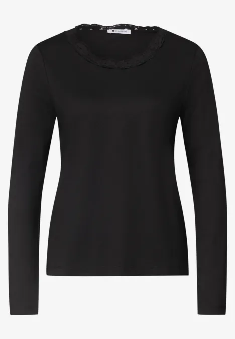 Schwarzes Langarmshirt mit Rüschen- und Spitzenbesatz am Rundhalsausschnitt.