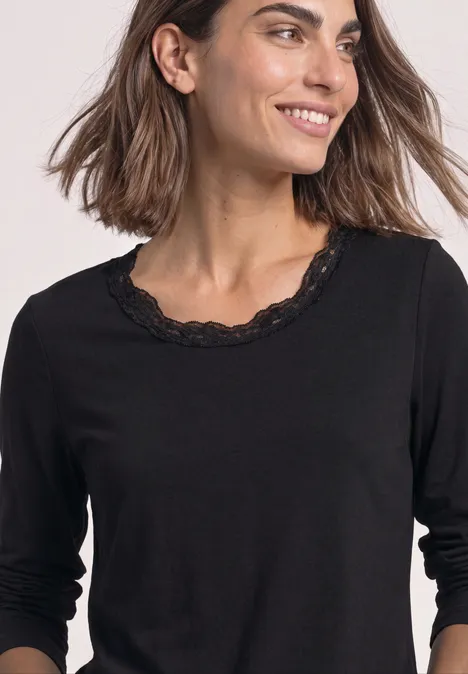 Frau trägt schwarzen 3/4-Arm-Pullover mit Spitzenbesatz am Rundhalsausschnitt.