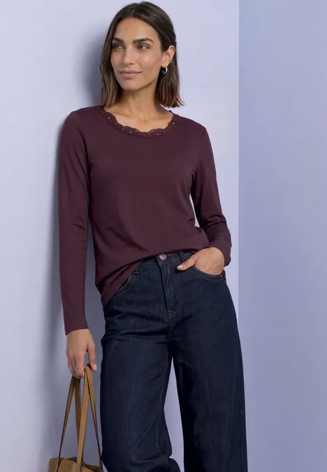 Langarm Shirt mit Rundhals und Spitze rustic rouge Frau in weinrotem Langarmshirt und dunklen, weiten Jeans hält eine Handtasche.