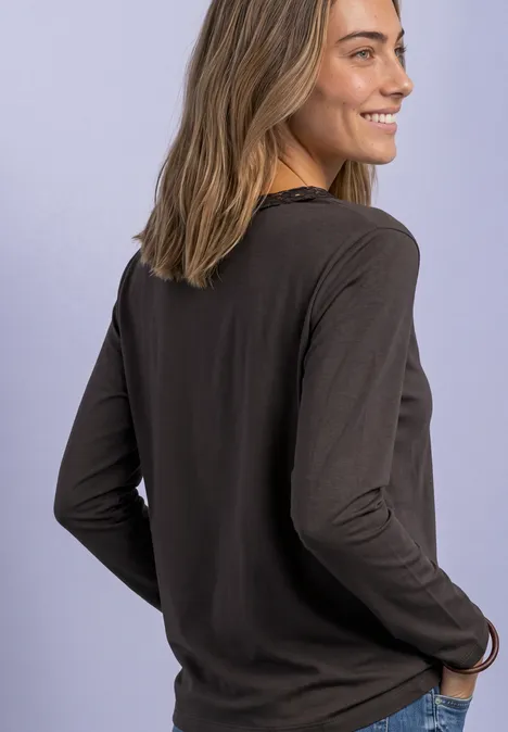 Junge Frau im Profil, lächelnd, in dunklem Langarmshirt vor hellem lila Hintergrund.