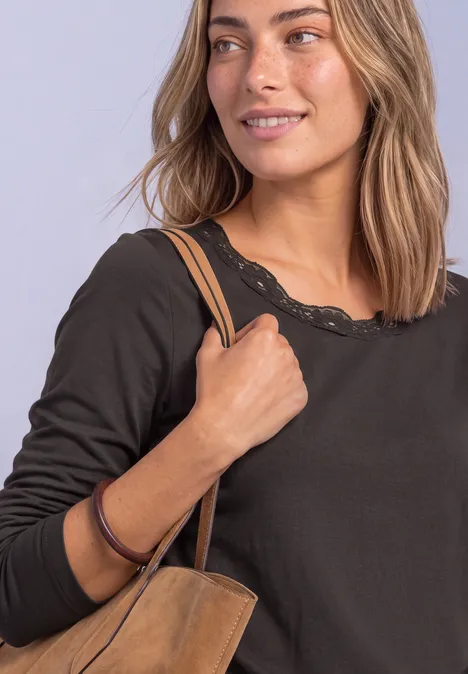 Frau in schwarzem Langarmshirt mit Spitzenkragen und brauner Schultertasche.