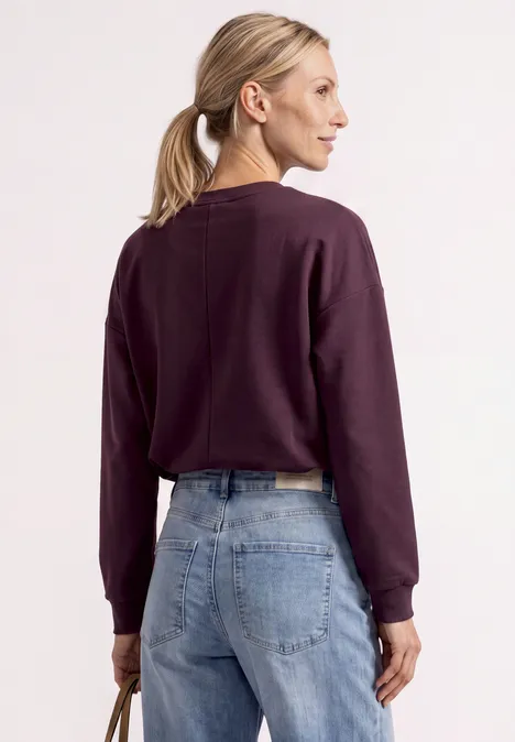 Frau mit Pferdeschwanz von hinten in lila Pullover und blauen Jeans.