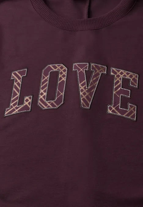Bordeauxfarbener Pullover mit dem Schriftzug LOVE in großen Blockbuchstaben und geometrischem Muster.