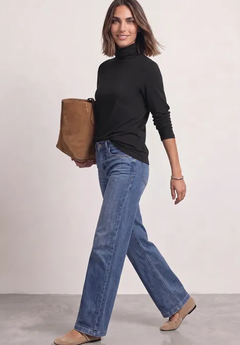 Langarm Shirt in Unifarbe mit Rollkragen Black Frau in schwarzem Rollkragenpullover und blauen Jeans mit brauner Tasche lächelnd.