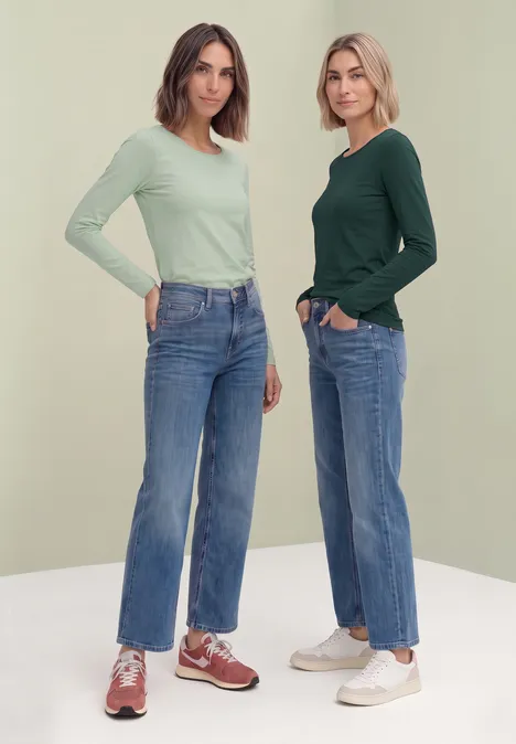 Lot de 2 t-shirts à manches longues et col rond shadow teal/eucalyptus green Zwei junge Frauen in Jeans, langärmligen Oberteilen und Sneakern vor hellem Hintergrund.