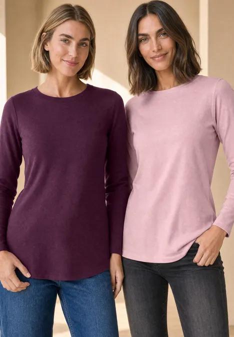 Twee vrouwen in casual mouwshirts en jeans lachen voor een lichte achtergrond.