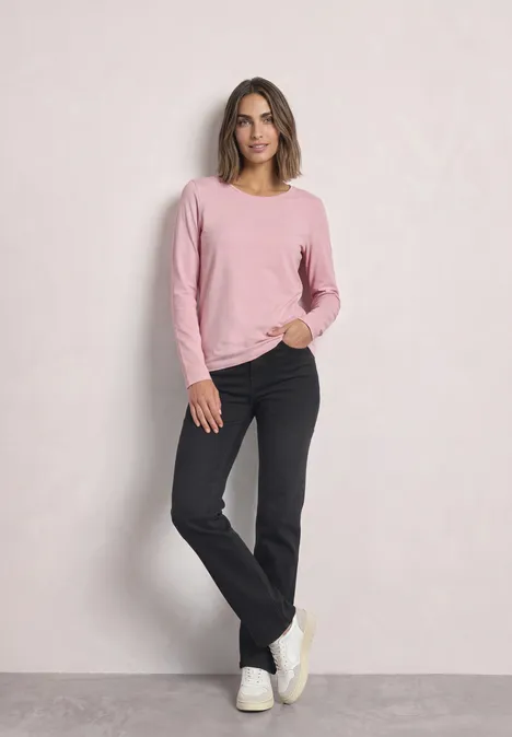 Lot de 2 t-shirts à manches longues et col rond berry maroon/quiet rose Frau in rosafarbenem Pullover und schwarzer Hose lehnt lässig an einer hellen Wand.