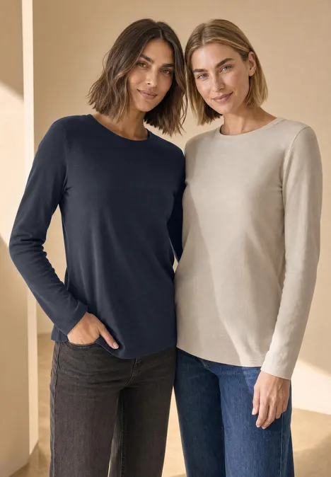 Twee vrouwen poseren naast elkaar in casual lange mouwen shirts en spijkerbroeken.