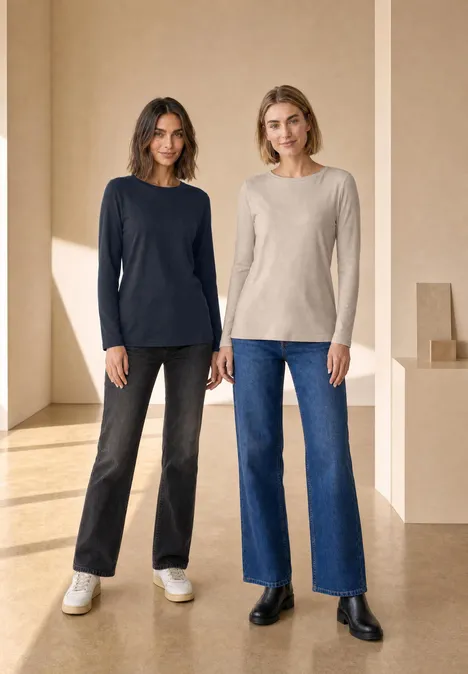 Twee vrouwen in een lichte ruimte dragen truien met lange mouwen en wijde jeans.