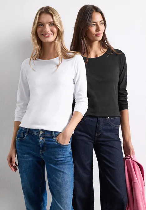 Shirts met lange mouwen en ronde hals, set van 2 stuks white/black Zwei Frauen in Jeans, eine mit weißem, die andere mit schwarzem Oberteil und rosa Jacke, stehen nebeneinander.