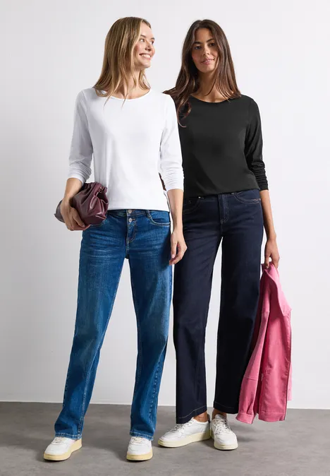 Shirts met lange mouwen en ronde hals, set van 2 stuks white/black Zwei lächelnde Frauen in Jeans und Langarmshirts, jeweils mit Jacke oder Tasche in der Hand.
