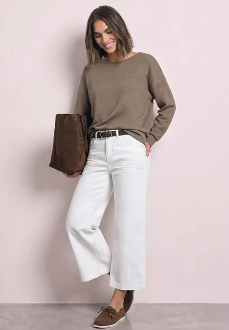 Frau mit taupefarbenem Pullover, weißen Culotte-Jeans und braunen Loafers, trägt braune Wildlederjacke.
