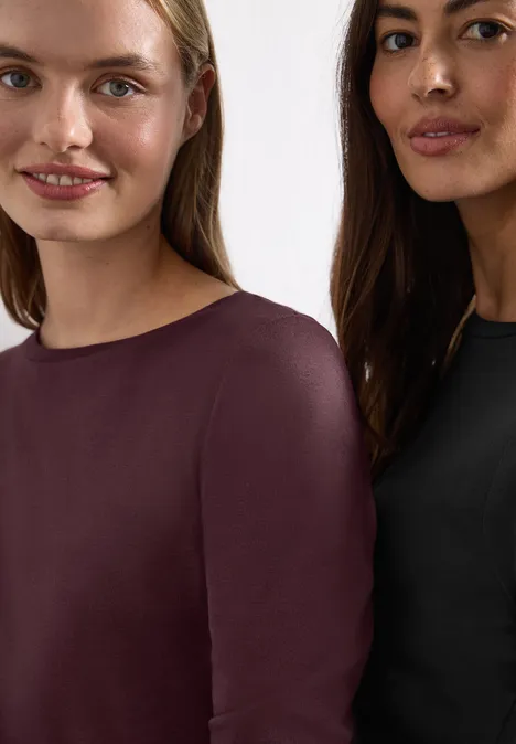 Langarm Shirts mit Boat Neck im 2er-Pack black/rustic rouge Zwei Frauen tragen schlichte Oberteile in Dunkelviolett und Schwarz, lächeln leicht und schauen zur Kamera.
