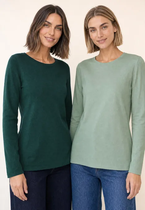 Twee vrouwen staan naast elkaar in lange mouwen truien, één donkergroen, de ander lichtgroen, beide met jeans.
