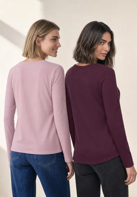 Zwei Frauen stehen Rücken an Rücken und tragen langärmelige Oberteile in Rosa und Dunkelrot.