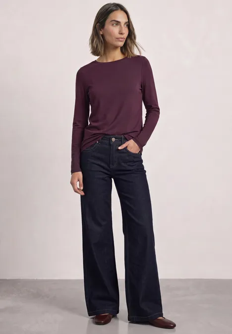 Lot de 2 t-shirts à manches longues et col bateau berry maroon/quiet rose Frau mit langärmeligem, weinrotem Oberteil und weiten Jeans steht vor hellem Hintergrund.