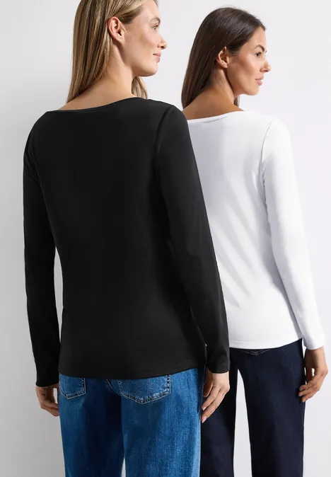 Shirts met lange mouwen en boothals, in een set van 2 stuks white/black Zwei Frauen stehen Rücken an Rücken, tragen schlichte Langarmshirts in Schwarz und Weiß sowie blaue Jeans.