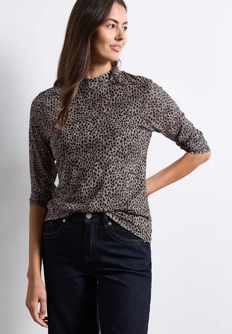 Mesh-Shirt met lange mouwen en col Black Frau in gepunktetem Rollkragenpullover und dunklen Jeans steht vor weißem Hintergrund.