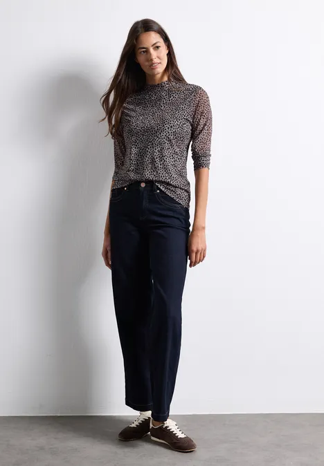 Mesh-Shirt met lange mouwen en col Black Eine Frau vor hellgrauer Wand trägt graues Leo-Top mit 3/4-Ärmeln, schwarze weite Hose und Sneaker.