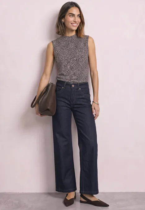 Frau in ärmellosem Leo-Top, weiten Jeans und schwarzen Ballerinas mit brauner Schultertasche.