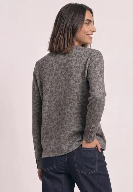 Rückenansicht einer Frau in grauem, gemustertem Strickpullover und dunkler Jeans.