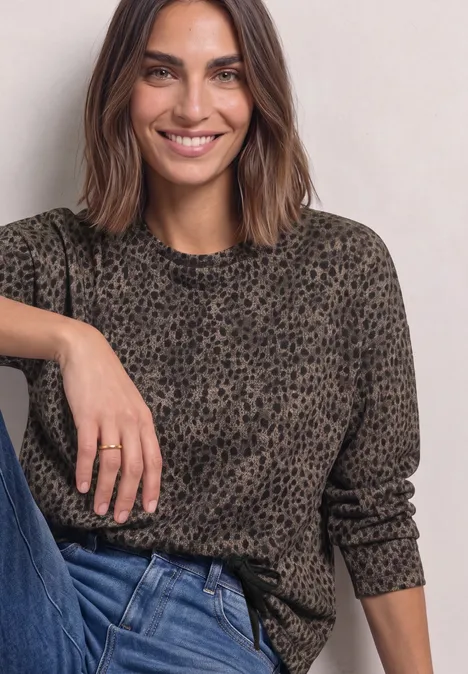 Shirt met lange mouwen, ronde hals en patroon Black Frau mit schulterlangen braunen Haaren in graubraunem Leopardenprint-Pulli und blauen Jeans lächelt.