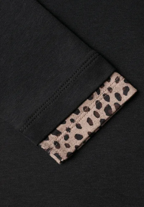 Zwart kledingstuk met een beige-zwarte luipaardprint mouwboordje dat subtiel uitsteekt.